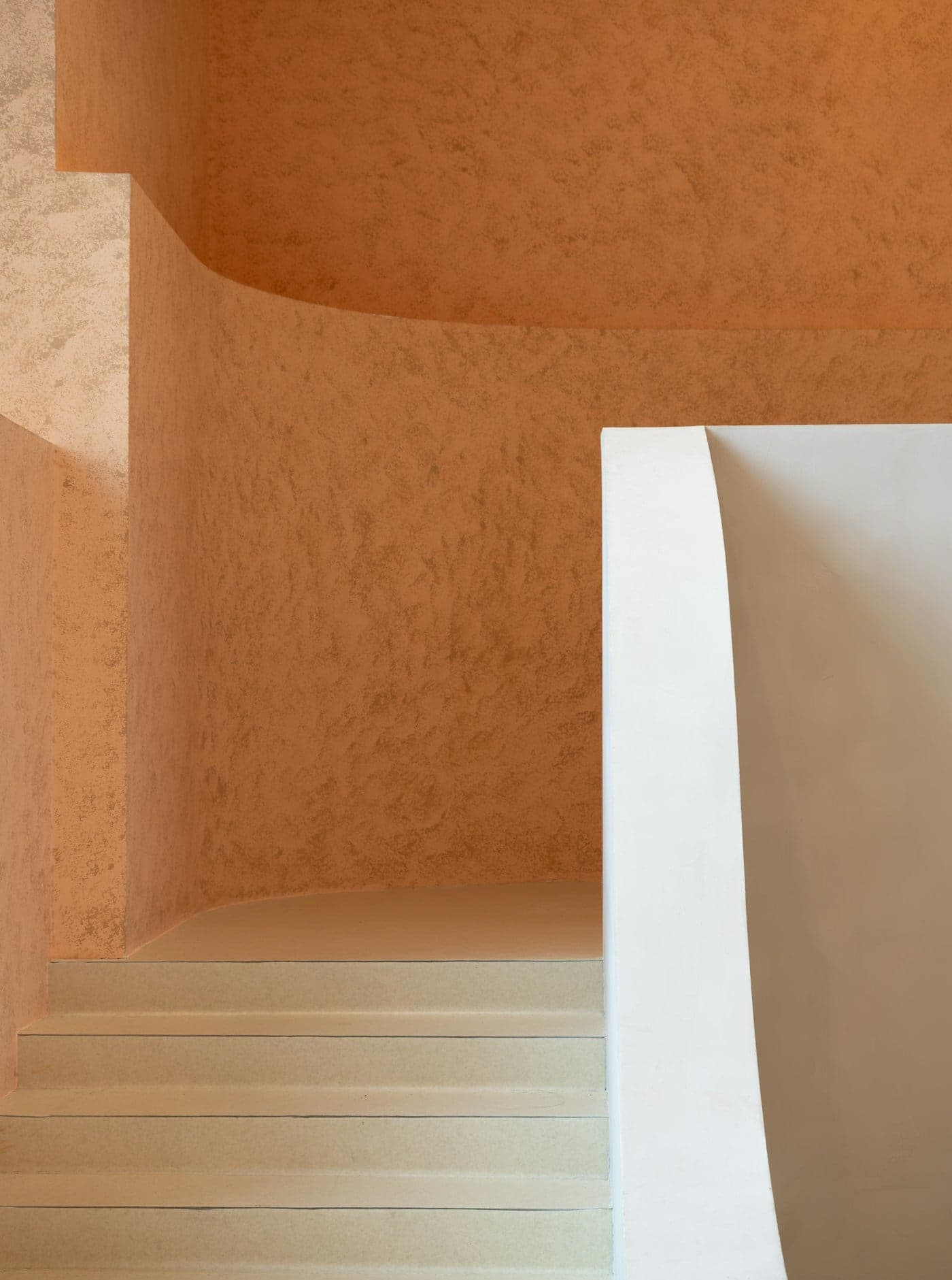 A sculptural curved wall in terracotta-toned textured plaster beside a white stair