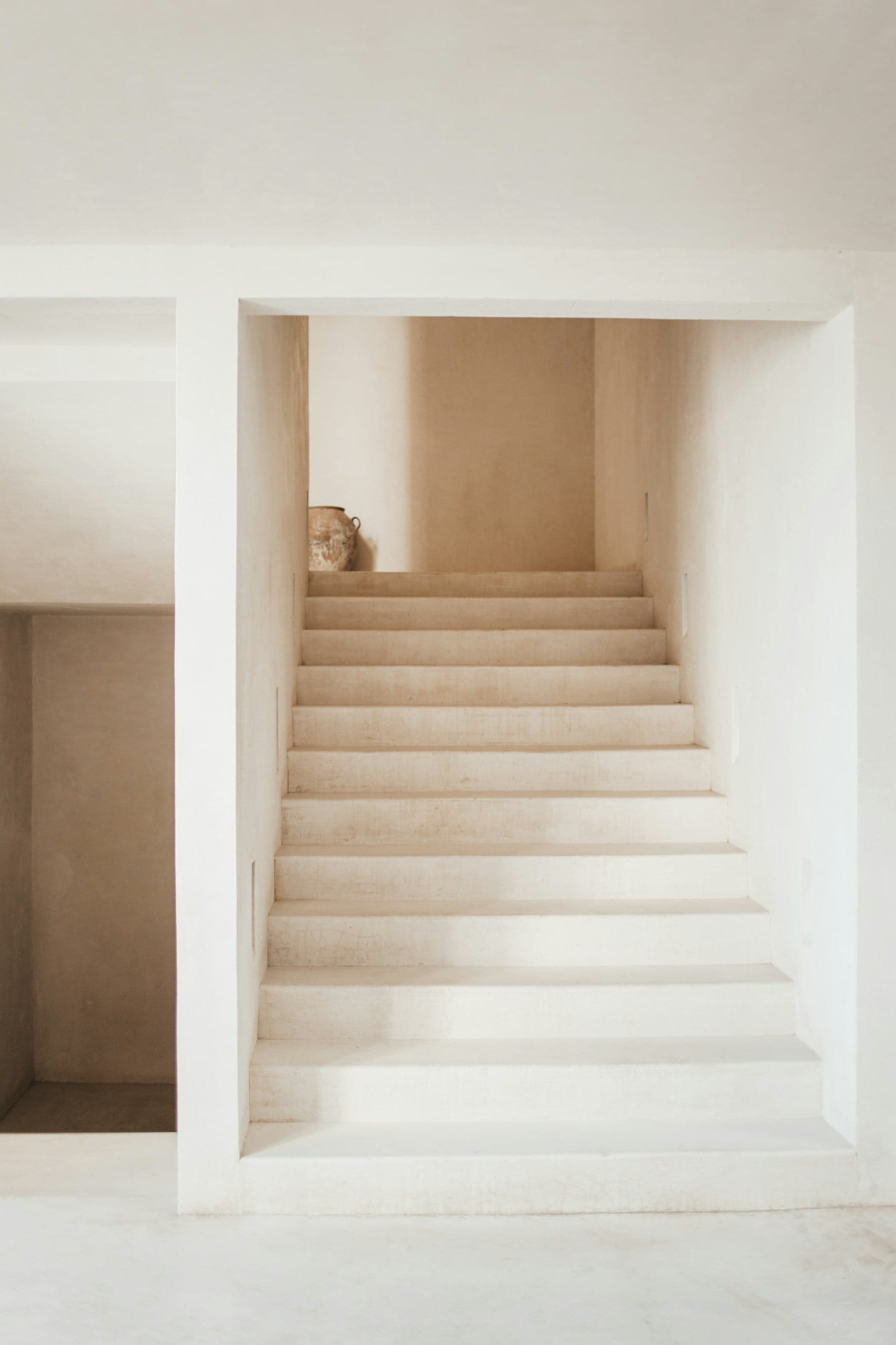 A minimalist staircase sculpted in seamless warm-white plaster